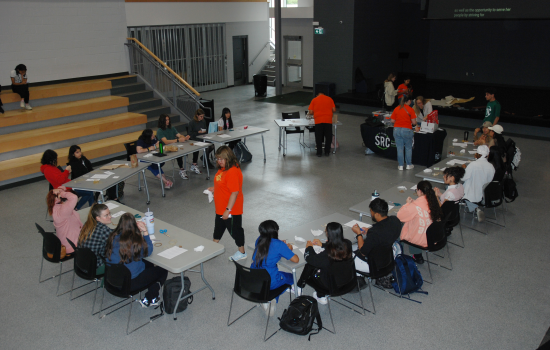 A view of the event, a circle of tables and chairs with students seated making dreamcatchers