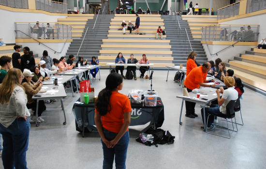 A view of the event, a circle of tables and chairs with students seated making dreamcatchers