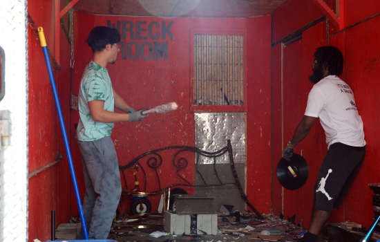 A student holding a baseball bat prepares to hit a record thrown by a staff member