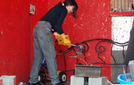 A student in the Wreck Room trailer wearing yellow gloves and holding an axe