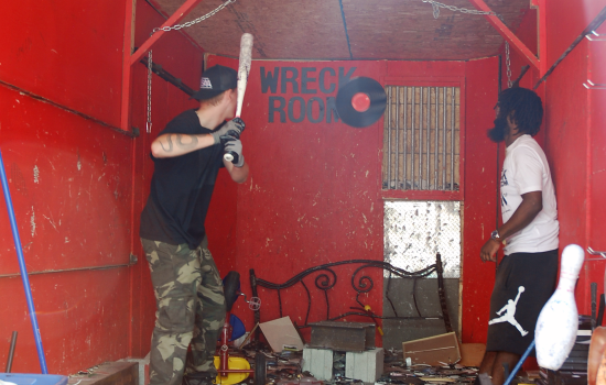 A student holding a baseball bat prepares to hit a record thrown by a staff member