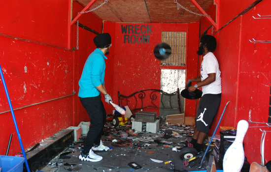 A student holding a baseball bat prepares to hit a record thrown by a staff member