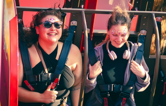 two students laugh and smile as they ride a swinging ride